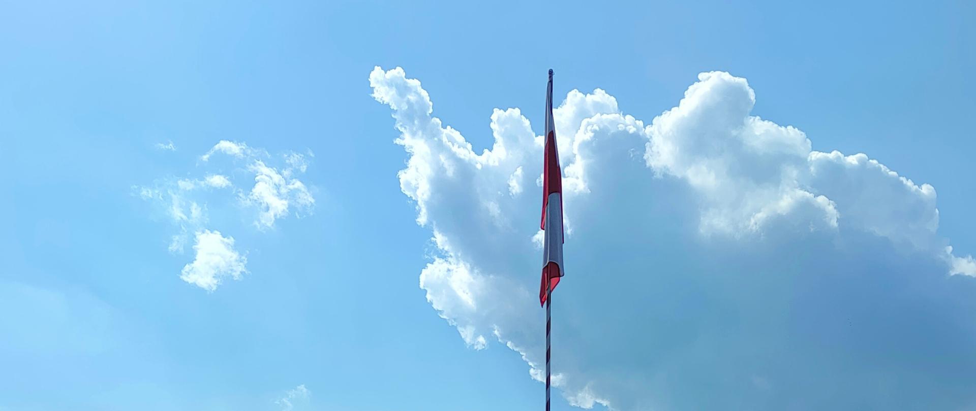 Na zdjęciu flaga państwowa Polski wciągnięta na maszt podczas uroczystej zbiórki z okazji Dnia Flagi. W tle budynek KP PSP w Strzyżowie.