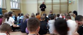 Na zdjęciu widać funkcjonariusza PSP ubranego w ubranie służbowe w trakcie pogadanki dla uczniów szkoły
podstawowej oraz przedszkola. Znajdują się na sali.