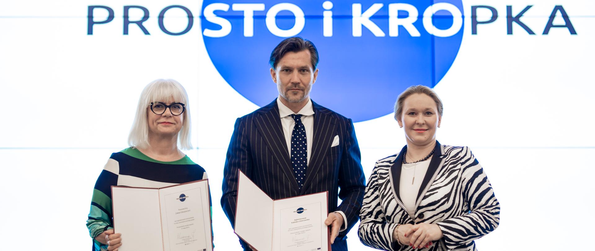 Przedstawicielka PZU, prezydent miasta Kalisz stoją i trzymają w ręku podpisane deklarację, obok stoi minister Możdżanowska. 