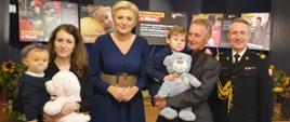 Na zdjęciu znajduje się Małżonka Prezydenta RP Agata Kornhauser-Duda razem z komendantem głównym PSP oraz rodziną zmarłego strażaka pozują do zdjęcia. W tle banery Fundacji 