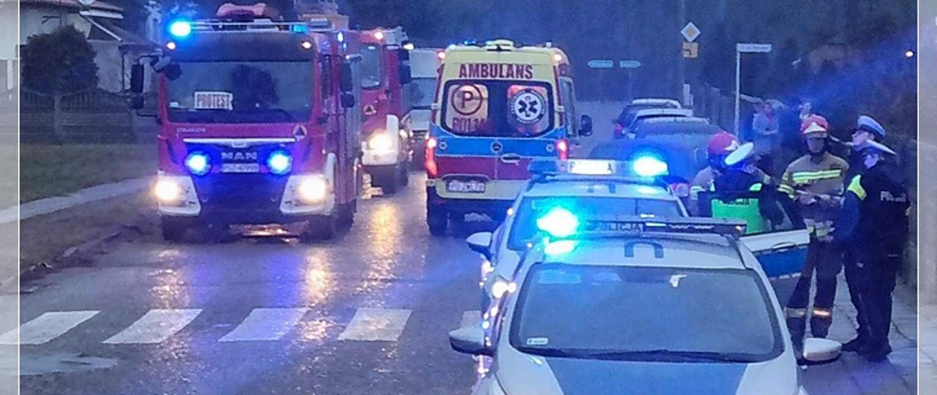 Widać przejście dla pieszych, przed przejściem samochód Policji, za przejściem samochody strażacki i karetka pogotowia