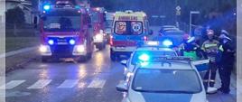 Widać przejście dla pieszych, przed przejściem samochód Policji, za przejściem samochody strażacki i karetka pogotowia