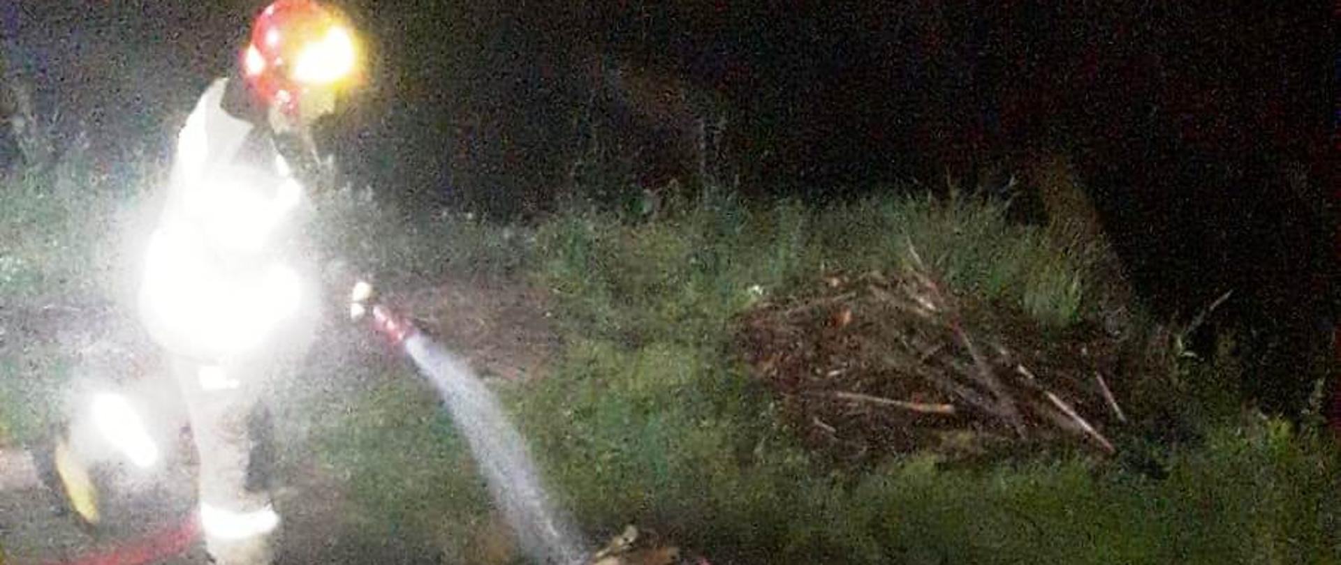 Spalone elementy mieszkania na zewnątrz budynku, które prądem wody gasi strażak.