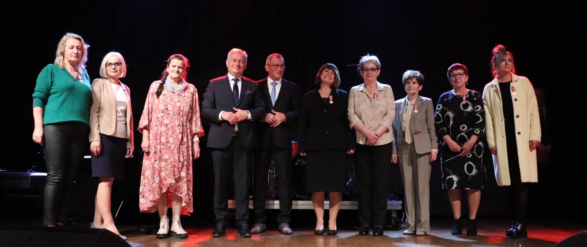 Grupa osób stojąca na scenie na czarnym tle