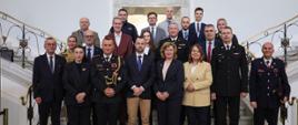 Delegacja Albanii oraz przedstawiciele PSP i administracji publicznej pozują do wspólnego zdjęcia na schodach w budynku instytucji państwowej.