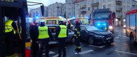 na zdjęciu widać dwa rozbite samochody osobowe oraz uszkodzony autobus komunikacji miejskiej. W tle dwie karetki pogotowia oraz wozy strażackie.