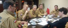 Widok ogólny. 5 funkcjonariuszy Państwowej Staży Pożarnej i 1 osoba siedzące przy stole omawiają wykonanie dokumentacji projektowej.