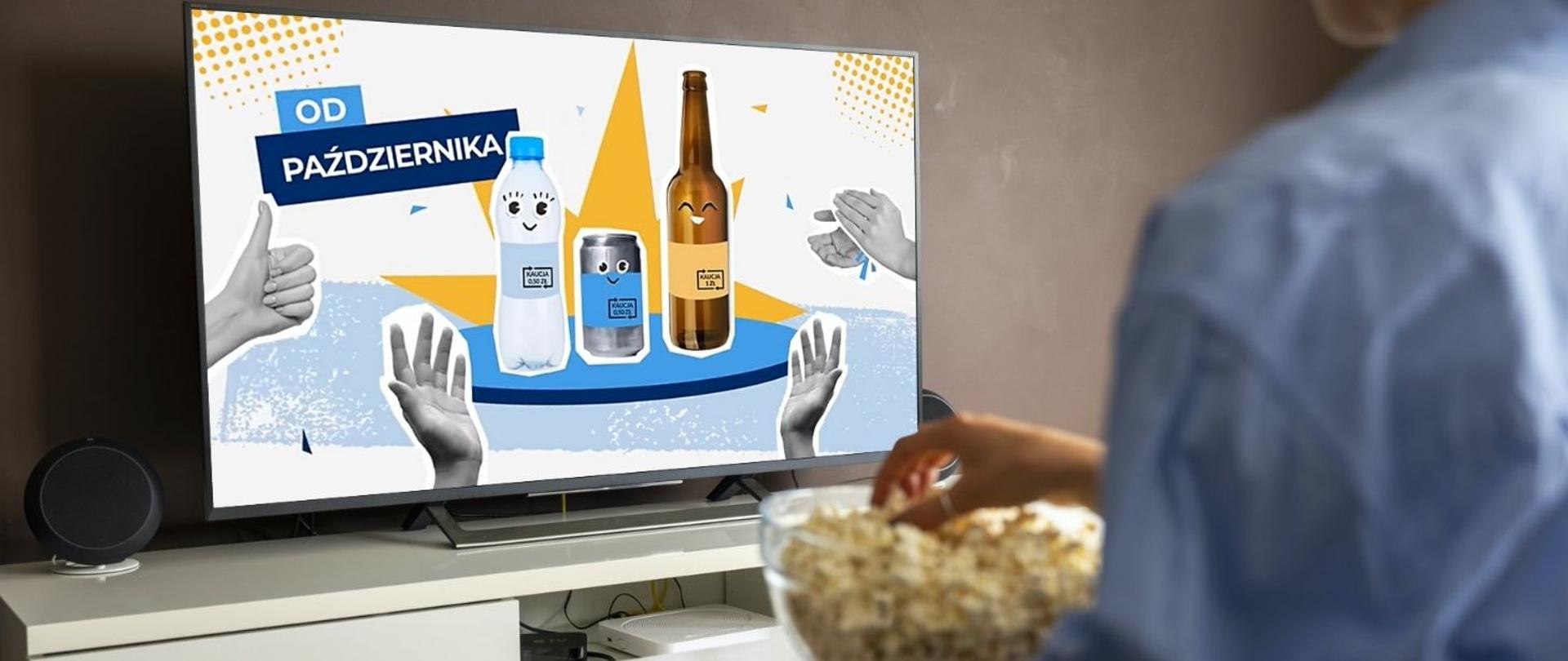 na zdjęciu widoczna jest postać, które siedzi na wprost telewizora, na którym wyświetlana jest reklama dot. systemu kaucyjnego. Postać ogląda reklamę i ręką sięga po popcorn do szklanej miski. 