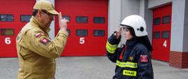 Widok z boku. Po prawej stronie komendant powiatowy PSP, który salutuje. Po prawej stronie druhna OSP salutująca po otrzymaniu zaświadczenia.