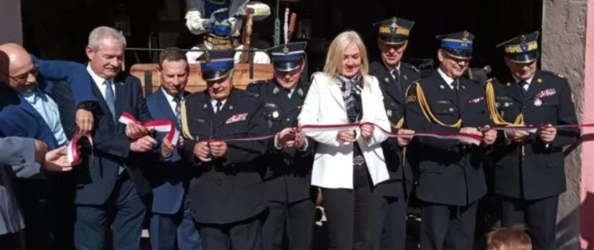 Obraz przedstawia przecięcie wstęgi na otwarciu Izby Pamięci