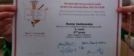 Zdjęcie przedstawia dyplom zdobyty na Międzynarodowym Interpretacyjnym Konkursie dla Instrumentów Dętych