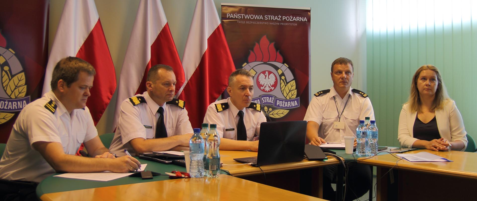 Wideokonferencja szefów służb pożarniczo-ratowniczych Polski i Litwy – na zdjęciu uczestnicy ze strony polskiej – nadbryg. Andrzej Bartkowiak komendant Główny PSP i nadbryg. Adam Konieczny zastępca komendanta głównego PSP oraz troje przedstawicieli Biura Współpracy Międzynarodowej KG PSP. Zdjęcie na tle trzech biało-czerwonych flag i logotypów PSP.