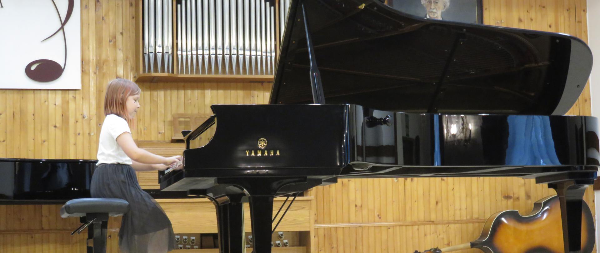 Uczennica siedzi przy fortepianie, w tle prospekt organów i kontrabas.