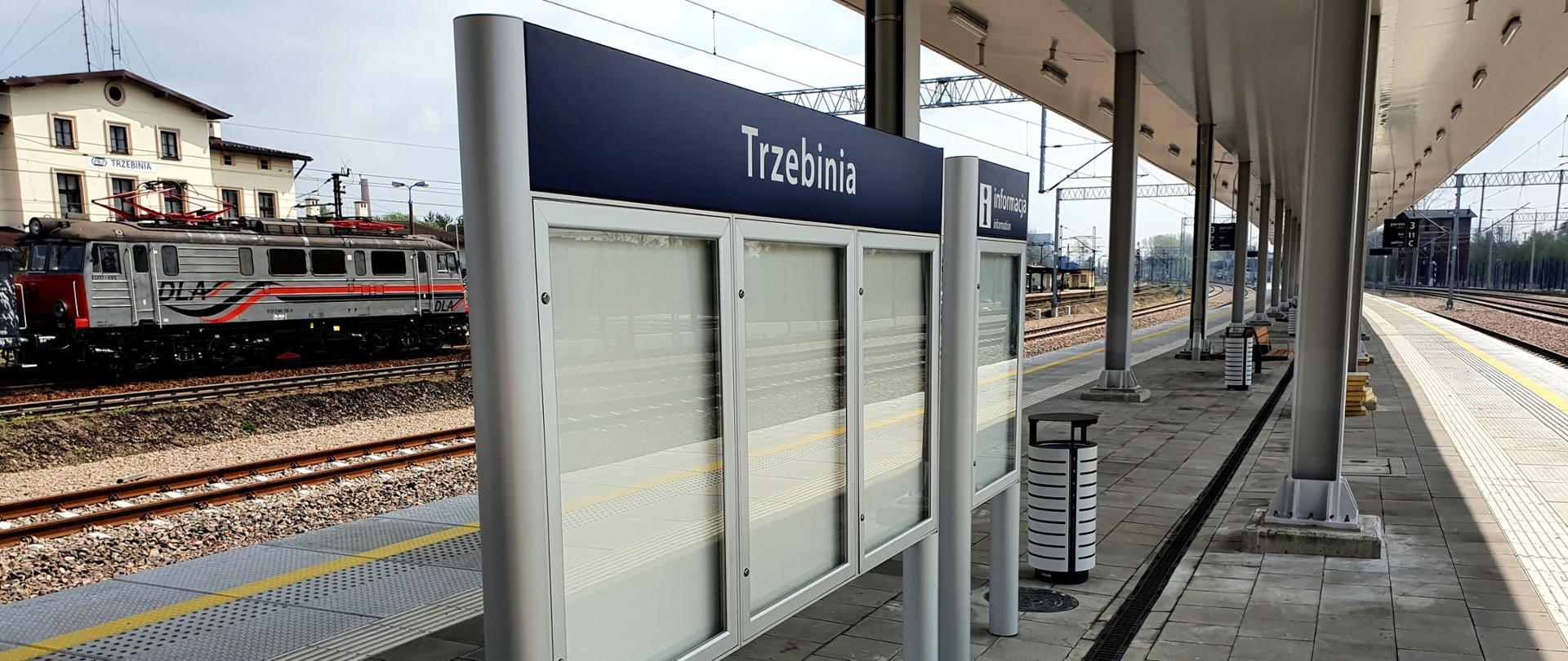 Na zdjęciu widać zmodernizowany peron kolejowy na stacji w Trzebinii. Po lewej stronie widać lokomotywę elektryczną. Pogoda jest słoneczna. 