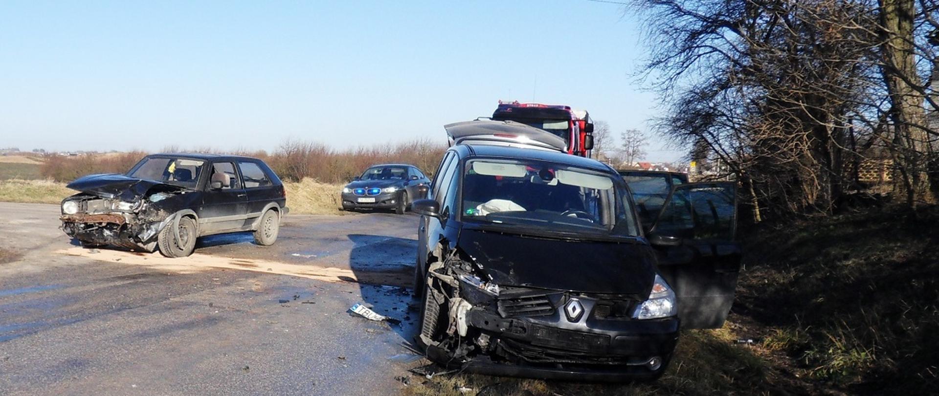 Zdjęcie przedstawia uszkodzone pojazdy na drodze w tle samochód pożarniczy i policja