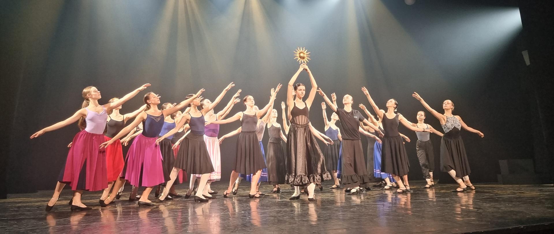 Balet Dworski „Cracovia Danza” – zawodowy zespół tańców dworskich i historycznych. Specjalizuje się w odtwarzaniu tradycyjnych tańców i baletów dworskich na przestrzeni wieków od średniowiecza po współczesność. Zdjęcie z warsztatów uczennic OSB 2023, lipiec. Przedstawia uczennice w trakcie ćwiczeń na sali baletowej w trakcie występu scenicznego. 