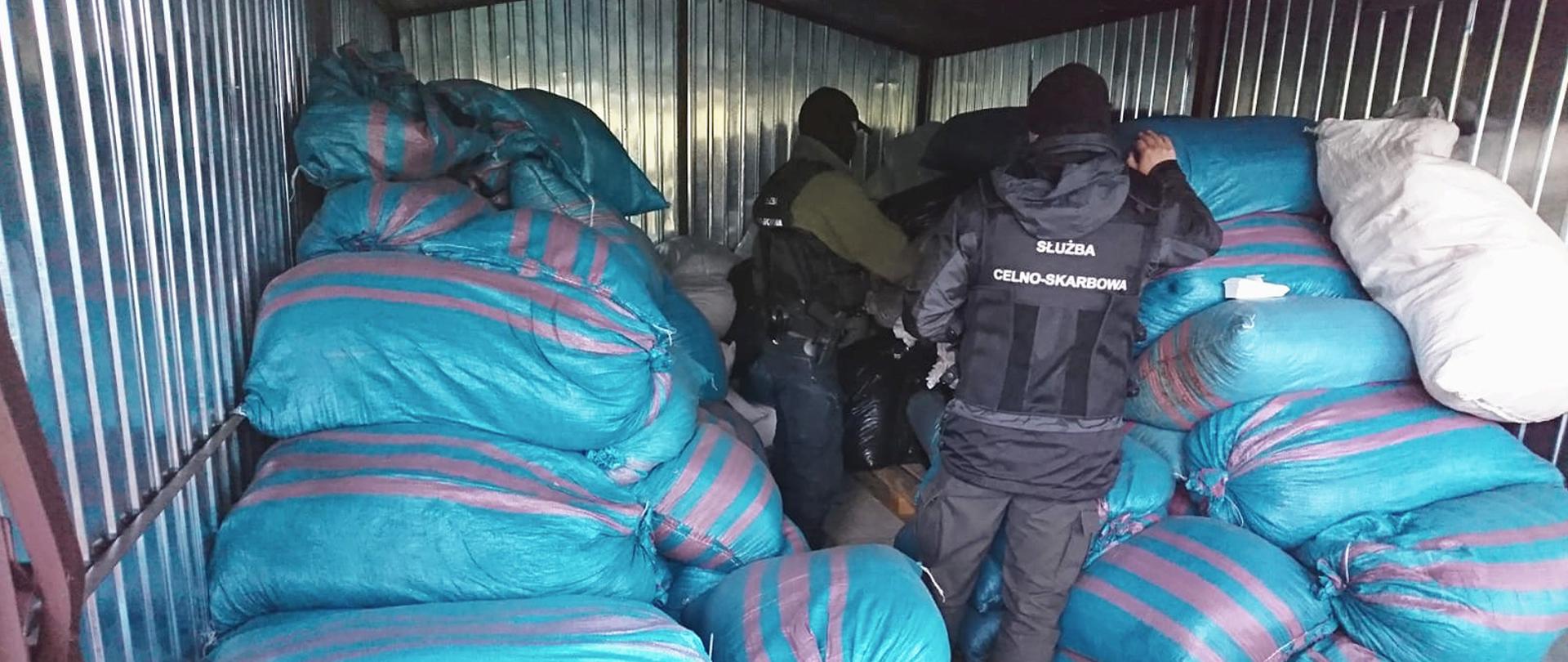 Funkcjonariusze Służby Celno-Skarbowej w pomieszczeniu z workami z wyrobami akcyzowymi.