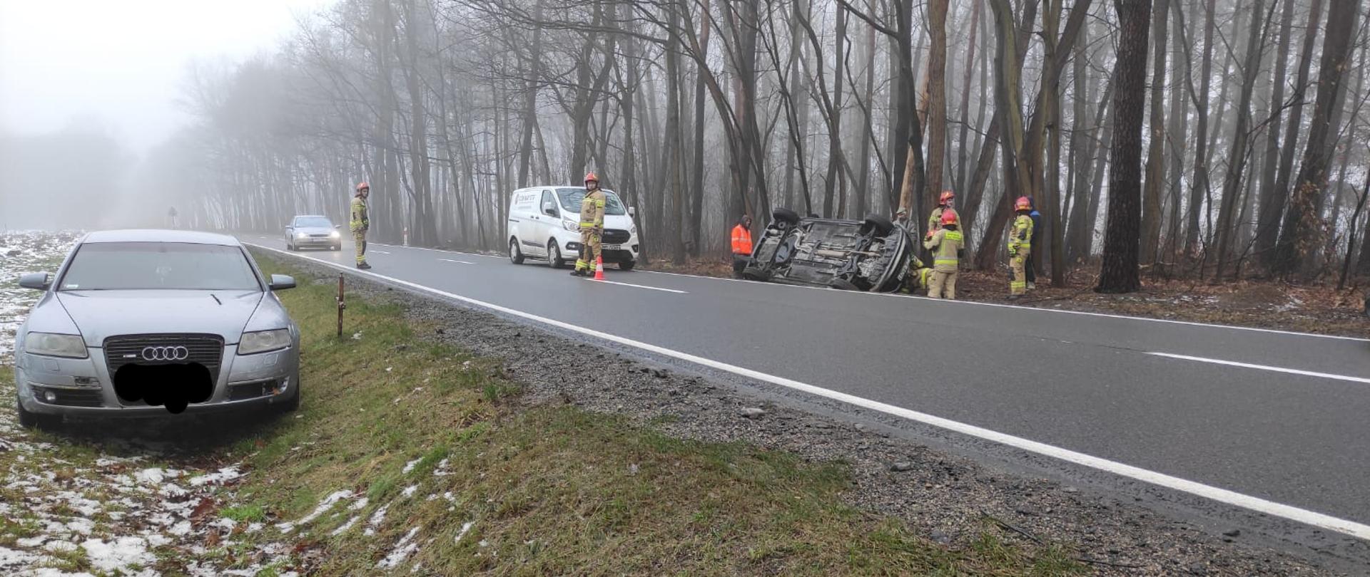 Na drodze krajowej numer dwanaście doszło do kolizji drogowej dwóch samochodów osobowych, wyniku której jedne z pojazdów dachował a drugi wjechał do rowu. Strażacy na drodze kierują ruchem drogowym i udzielają pomocy osobą poszkodowanym.