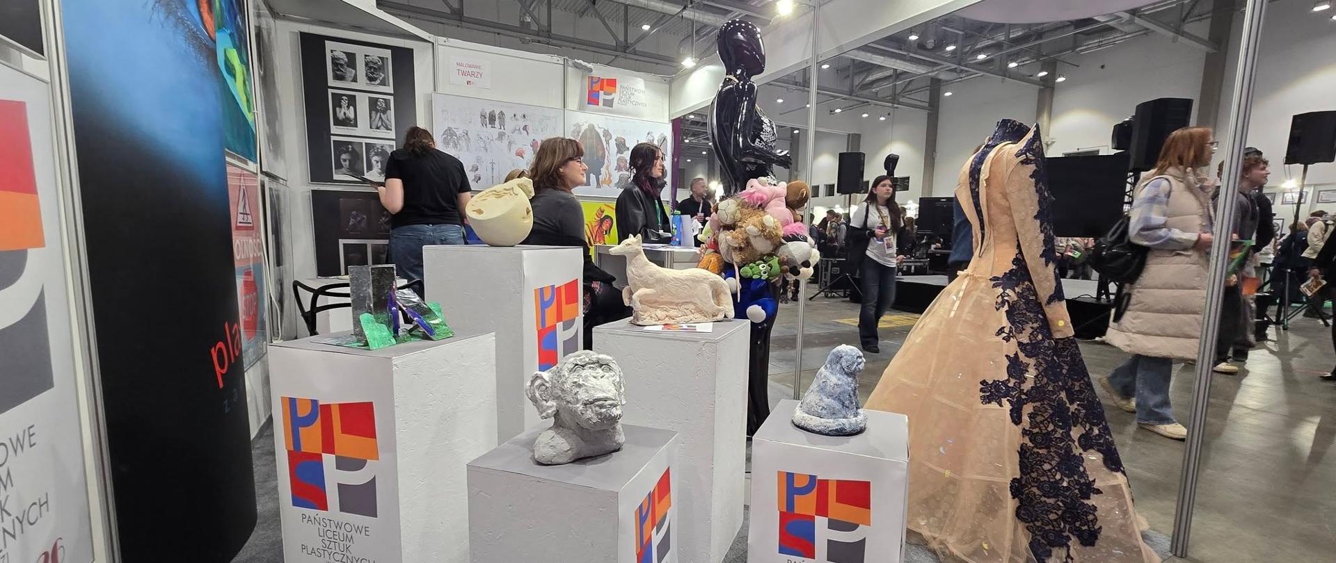 stoisko na targach edukacyjnych, na pierwszym planie kubiki z rzeźbami oraz manekin w długiej, balowej sukni
