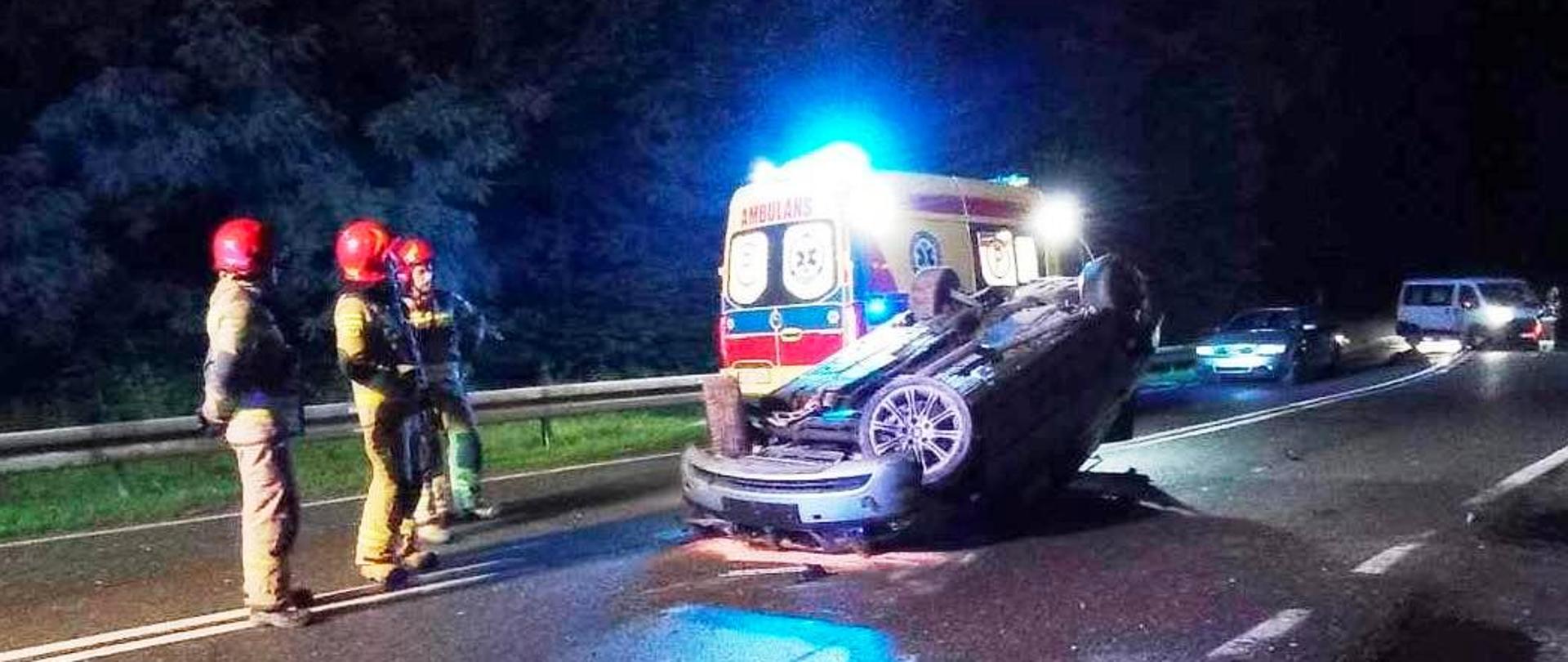 Strażacy przy samochodzie, który dachował na drodze