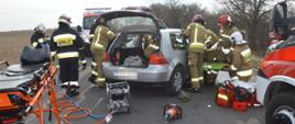 Zderzenie dwóch aut. Okolice Zaborowic. Odcinek jezdni, na którym doszło do wypadku. Strażacy wykonują dostęp do osób znajdujących się w volkswagenie stojącym na środku drogi. Mają przygotowane nosze-deskę ortopedyczną, przy pomocy której będą ewakuować pasażera golfa. Przed samochodem znajduje się sprzęt hydrauliczny, a obok nosze z karetki pogotowia.