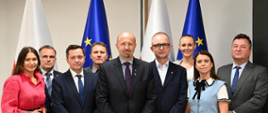 Na zdjęciu od lewej: Monika Flisek, Zastępca Dyrektora Departament Adaptacji do Zmian Klimatu NFOŚiGW; Jacek Drabiński, Zastępca Dyrektora Regionalnego Zarządu Gospodarki Wodnej we Wrocławiu ds. Ochrony Przed Powodzią i Suszą; Mateusz Balcerowicz, Prezes Państwowego Gospodarstwa Wodnego Wody Polskie; Bogdan Zakrzewski, Zastępca Dyrektora ds. Ochrony Przed Powodzią i Suszą RZGW Szczecin; Robert Gajda, Zastępca Prezesa Zarządu NFOŚiGW, Krzysztof Pałka, Przewodniczący Rady Nadzorczej NFOŚiGW; Marta Barszczewska-Skąpska, Dyrektor Departamentu Inwestycji i Renaturyzacji w Państwowym Gospodarstwie Wodnym Wody Polskie; Agnieszka Siłacz, Dyrektor Regionalnego Zarządu Gospodarki Wodnej w Bydgoszczy; Robert Markiewicz, Dyrektor Departament Adaptacji do Zmian Klimatu NFOŚiGW. Pod zdjęciem widoczne są logotypy Funduszy Europejskich, Rzeczypospolitej Polskiej, Unii Europejskiej i NFOŚiGW.