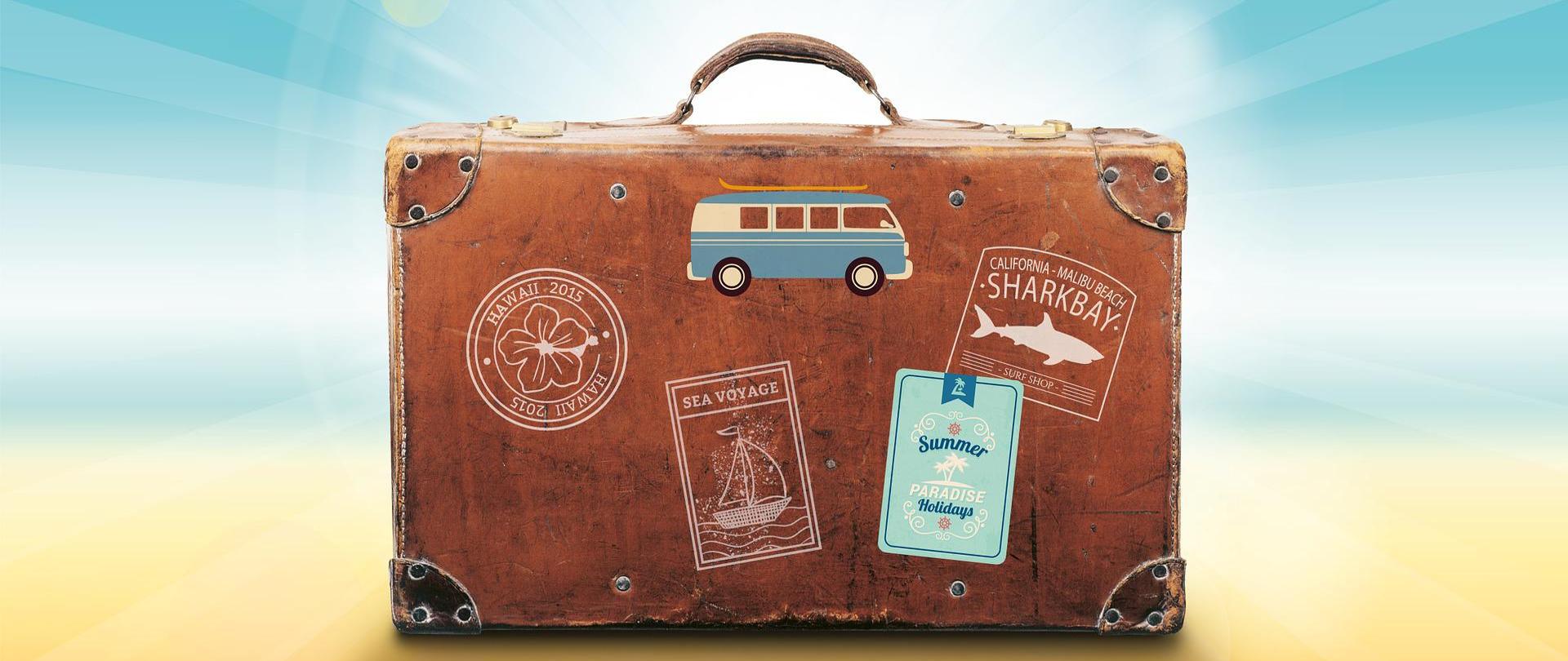 Rozświetlone niebiesko żółte tło. Brązowa walizka w stylu retro z naklejkami i stemplami.