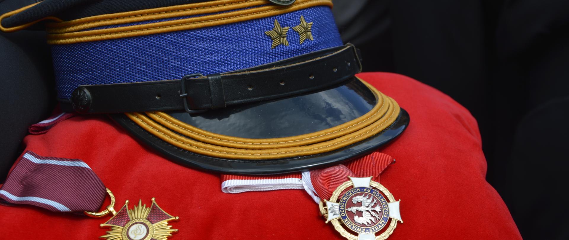 Na zdjęciu widać rogatywkę PSP brygadiera oraz dwa medale które leżą na czerwonej poduszce. 