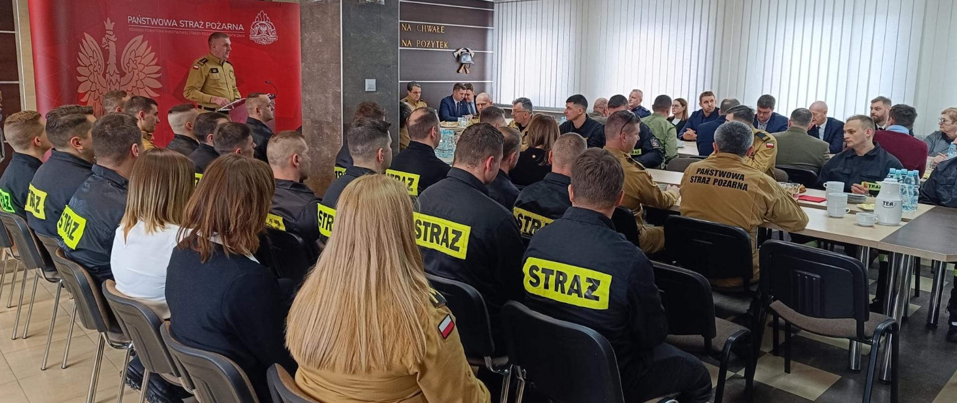 19 lutego 2026 r. w siedzibie Komendy Powiatowej Państwowej Straży Pożarnej w Siemiatyczach odbyła się coroczna odprawa podsumowująca stan bezpieczeństwa pożarowego na terenie powiatu siemiatyckiego w 2025 roku - sala pełna zaproszonych gości i funkcjonariuszy, przy mównicy stoi komendant powiatowy