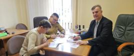 Przedstawiciele Państwowej Straży Pożarnej i partnerów instytucjonalnych podpisują dokumenty podczas spotkania roboczego w gabinecie.