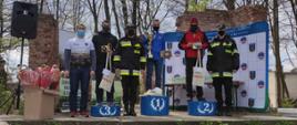 Na zdjęciu widać strażaków, zwycięzców biegu na orientację. Stoją na podium z otrzymanymi pucharami. 