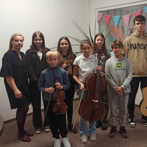 Zdjęcie przedstawia siedmioro uczniów w pozycji stojącej, wraz z nauczycielką. Uczniowie pozują do zdjęcia trzymając instrumenty muzyczne.