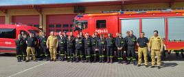 Uczestnicy szkolenia po zakończonych egzaminach stoją w dwuszeregu na tle s=dwóch samochodów pożarniczych.