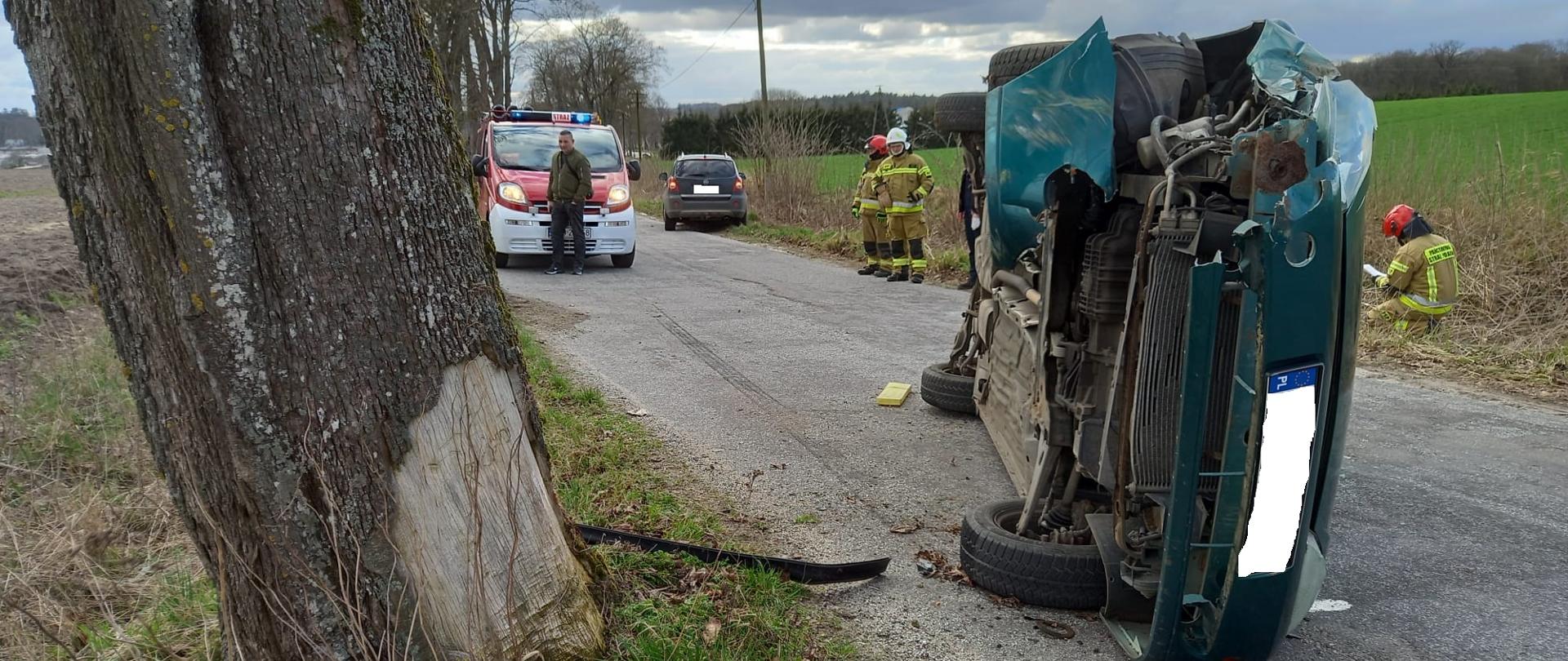 Zdjęcie przedstawia zielony samochód osobowy leżący na boku na jednym pasie jezdni blokując go.