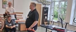 Prowadzący pokazuje jak stosować opaskę uciskową na udzie. Wokół siedzą uczestnicy Warsztatów Terapii Zajęciowej Caritas Archidiecezji Białostockiej