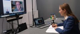 Minister funduszy i polityki regionalnej Katarzyna Pełczyńska-Nałęcz siedzi przy stole, przed nią laptop na którego ekranie widać mężczyznę