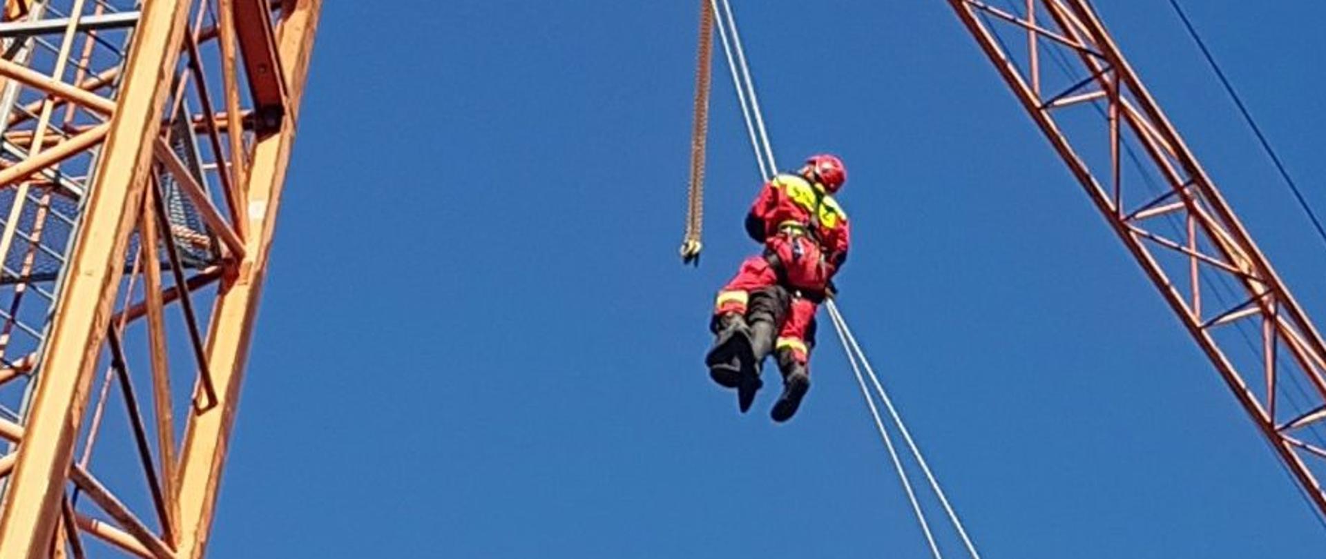 Dźwig budowlany - żuraw, po linie zjeżdżają dwie osoby
