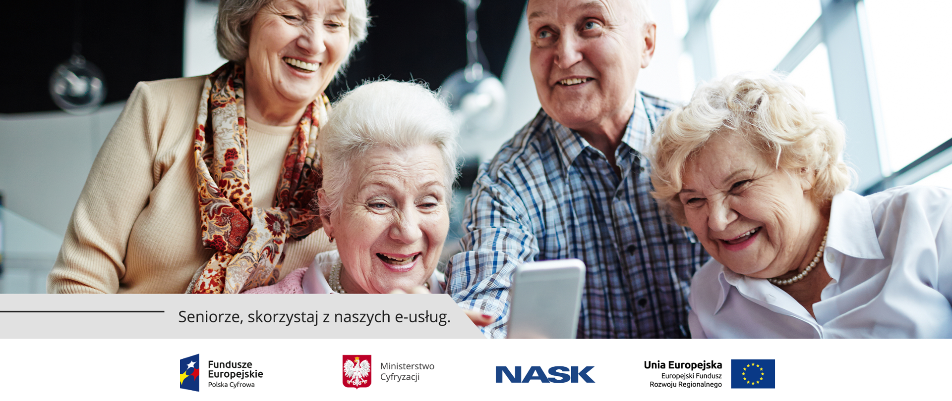 Czworo uśmiechniętych seniorów patrzy ekran telefonu.