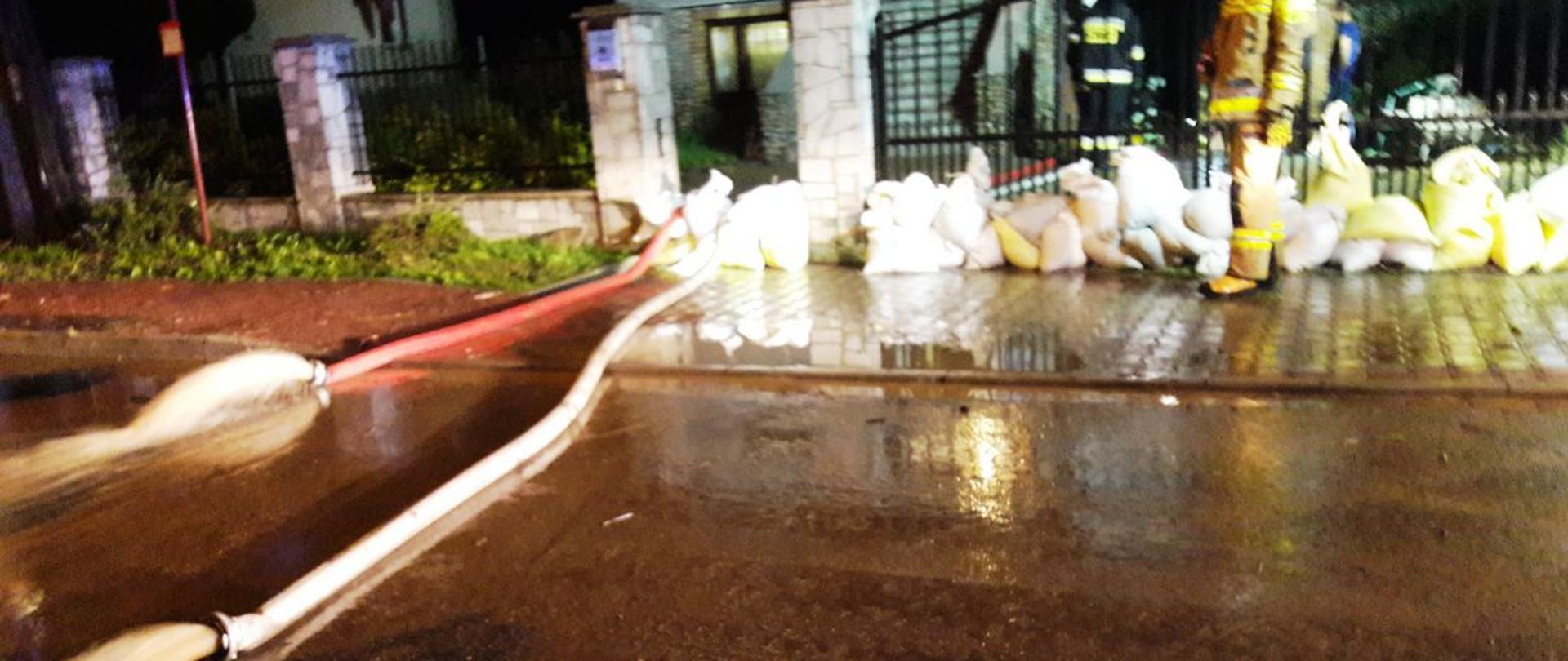 Strażacy wypompowują wodę z posesji obstawionej workami z piaskiem.