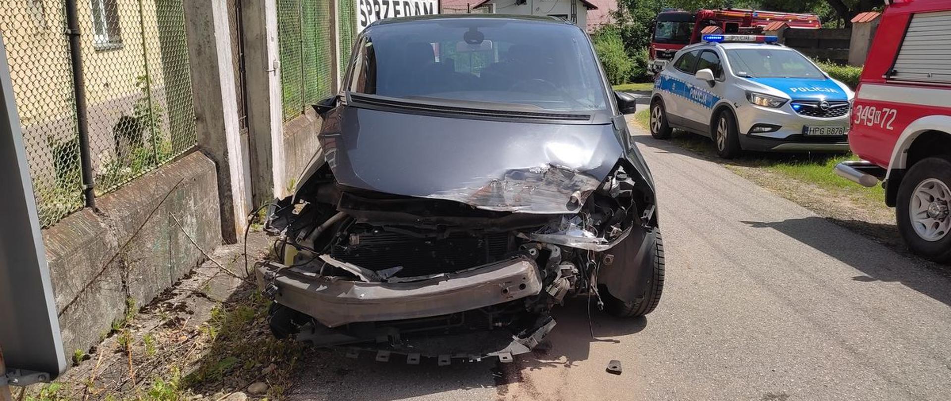 Rozbity samochód na drodze przed przejazdem a obok samochód Policji.