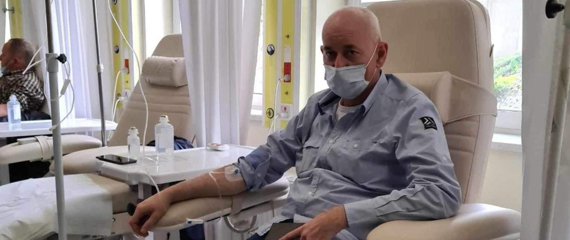 Zdjęcie przedstawia strażaka.
W tle pomieszczenie w szpitalu.
