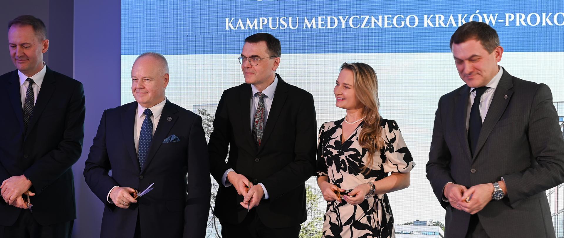 Przed rozciągniętą wstążką stoi pięć osób, drugi od lewej wiceminister Gzik, wszyscy trzymają nożyczki.