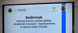 Slajd na ekranie konferencyjnym z napisem: Konferencja „Ochrona ludności, obrona cywilna, zarządzanie kryzysowe – bezpieczeństwo w regionie Żuław i Powiśla”