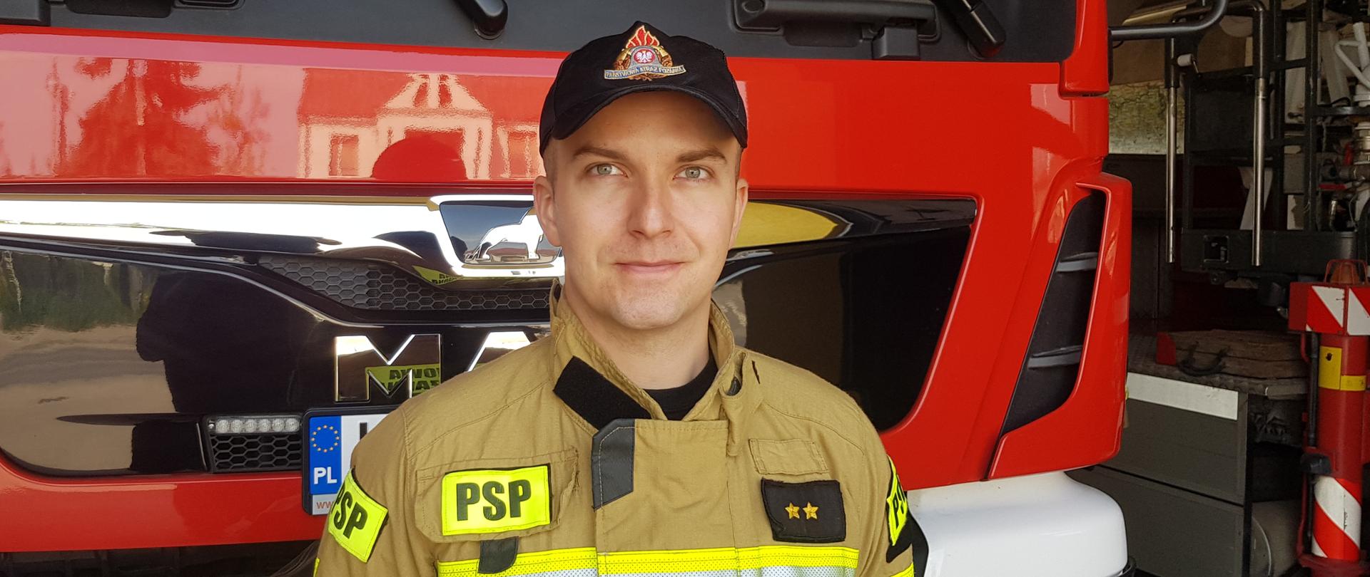 Portret strażaka w ubraniu specjalnym na tle samochodu pożarniczego
