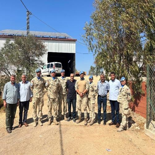 Grupa osób, w tym żołnierzy, pozuje do zdjęcia przez budynkiem sortowni odpadów