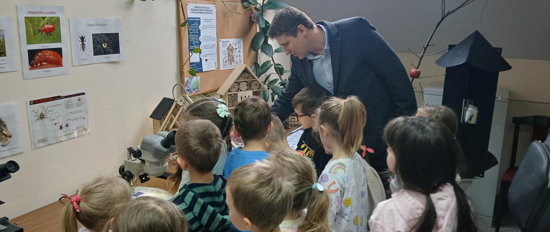 Grupa dzieci przyglądająca się przedmiotom widocznym na stole i mężczyzna prezentujący
