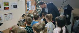 Grupa dzieci przyglądająca się przedmiotom widocznym na stole i mężczyzna prezentujący