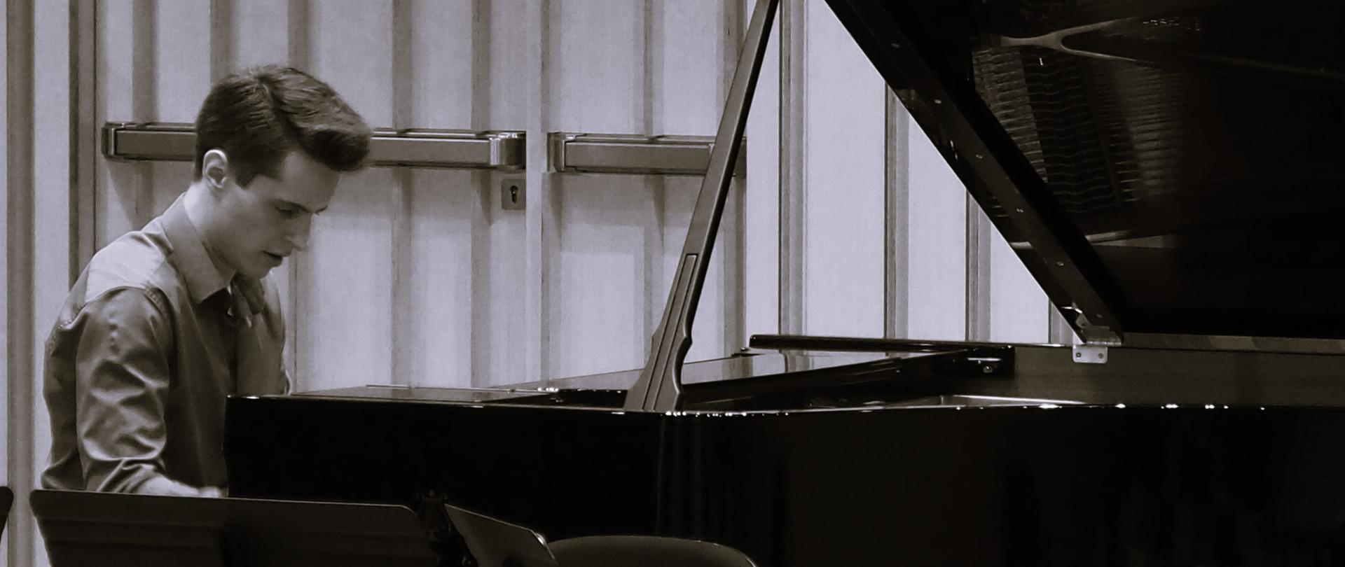 Czarno - biała fotografia pianisty grającego na fortepianie w sali koncertowej.