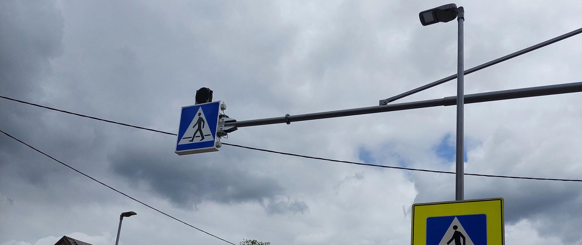 Latarnie uliczne i znaki drogowe wskazujące na przejście dla pieszych.