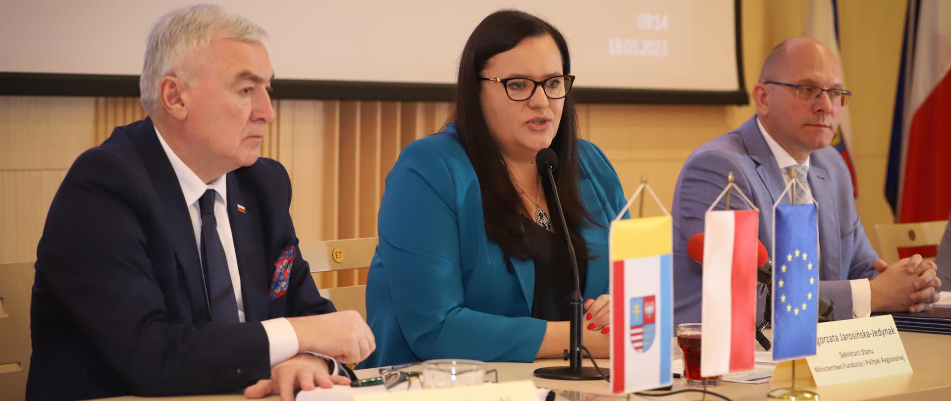 Trzy osoby siedzą przy stole. W środku siedzi wiceminister Małgorzata Jarosińska-Jedynak.